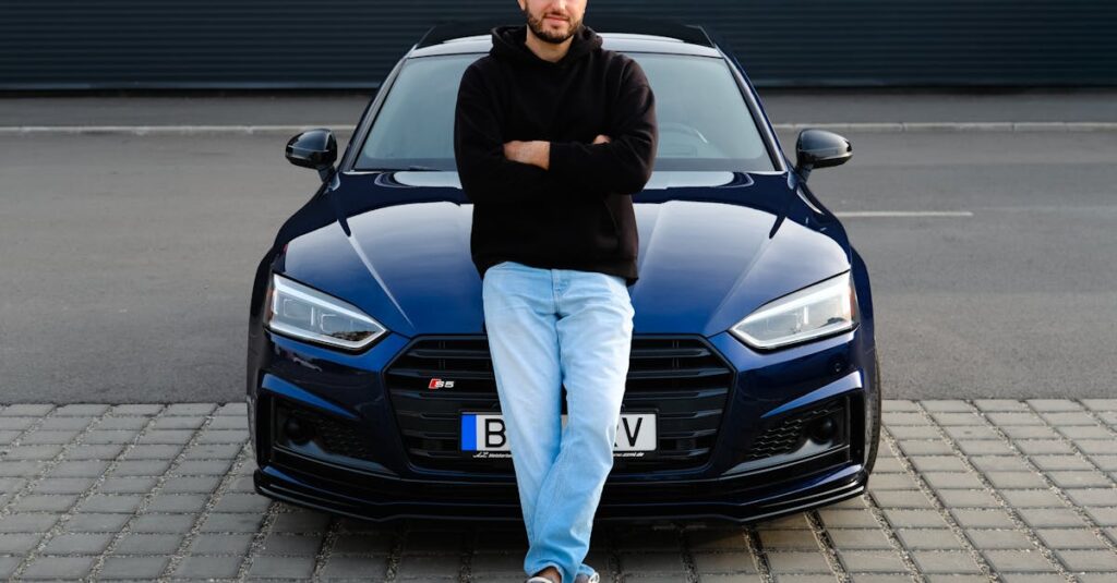 Man casually leaning on a blue car on a street, displaying urban fashion and style.